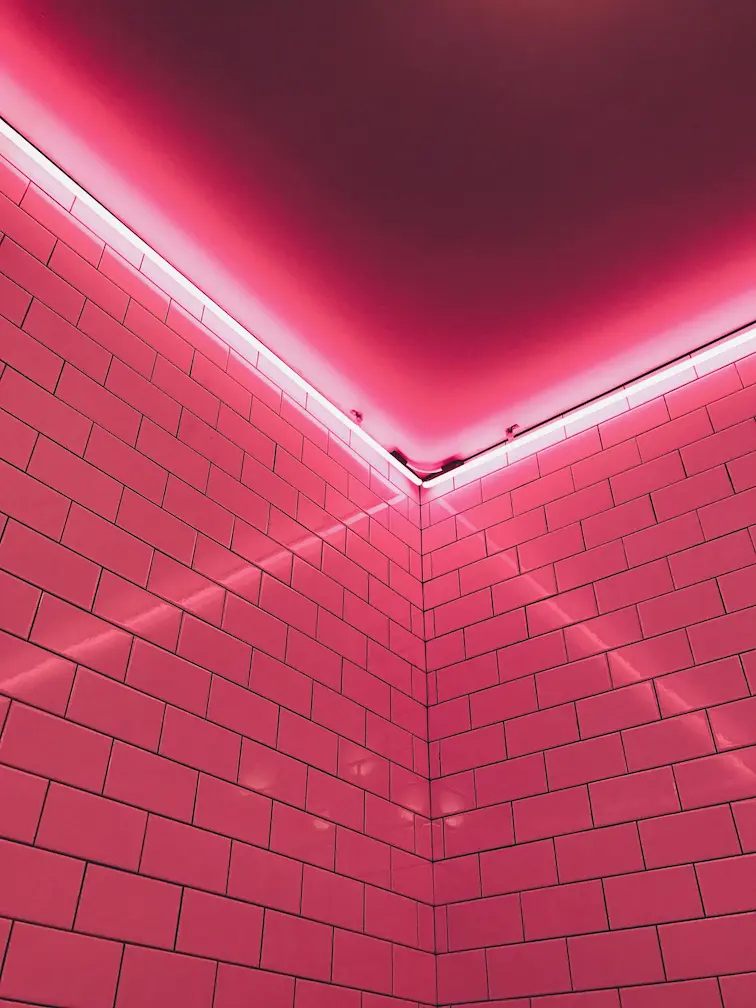 a picture of a room corner, washed in pink light from neon tubes.